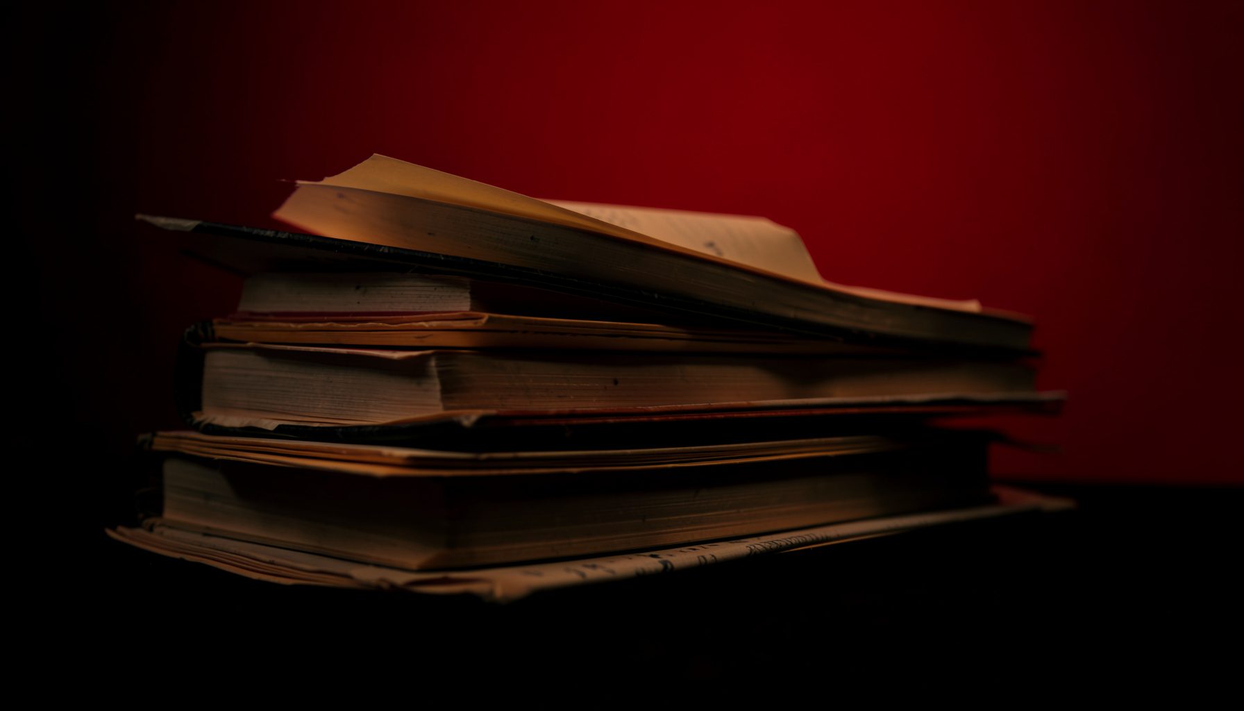 Stacked books and pages in soft warm light against a near-black background