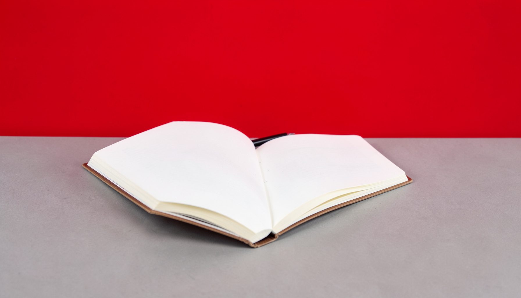 An open notebook and pen on a warm grey surface, suggesting announcements and written updates